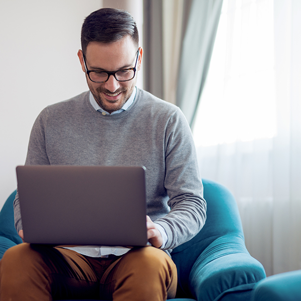 Handsome man using a laptop while sitting on armchair at home.