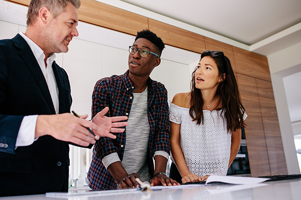 Interracial couple having consultation with a real estate agent inside a new home. Mature male realtor discussing the contract with customer.