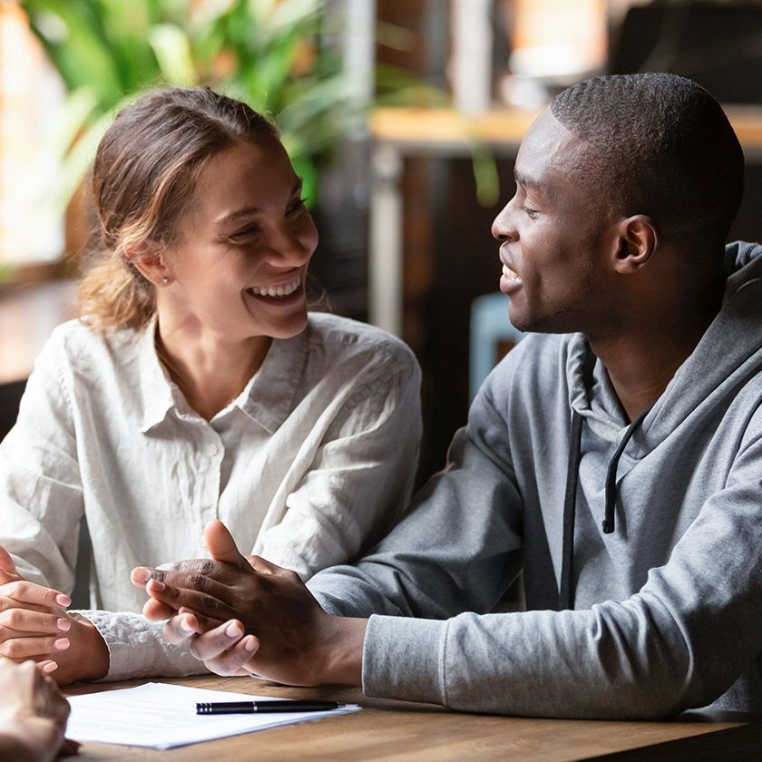 Smiling young mixed ethnicity couple talk decide on financial mortgage deal consider insurance loan meeting bank manager, female insurer consult interracial customers offer contract, business advice